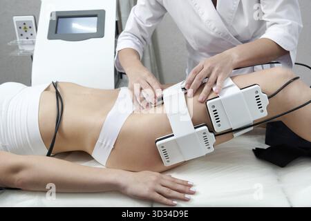 Belle femme obtenant la thérapie d'électro stimulation. Équipement laser lipo. Traitement cosmétique de réduction de graisse. Femme dans le salon de médecine. Proc. Anti-cellulite Banque D'Images