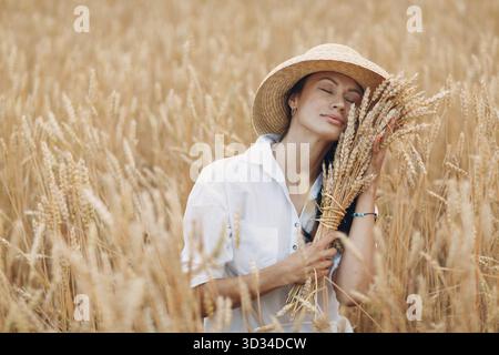 Jeune femme en chapeau de paille tenant une feuille d'épis de blé au champ agricole Banque D'Images