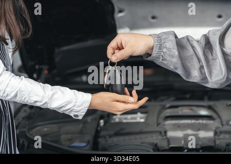 Mécanicien de voiture donnant les clés du client à sa voiture réparée dans le service de réparation automobile Banque D'Images
