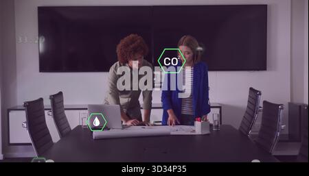 Deux collègues se penchant sur la table dans la salle de conférence, examinant les plans avec l'ordinateur portable et les données de CO2 Banque D'Images