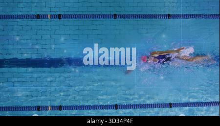 Femme de natation effectuant le crawl avant dans la piscine pour longueurs, avec séparateurs de voie, bande, casquette rose et lunettes Banque D'Images