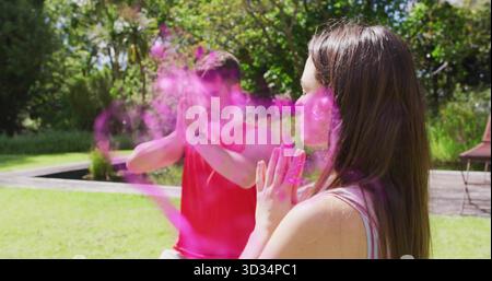 Assis couple méditant dans des vêtements de sport sur la pelouse herbeuse près de l'élément d'eau, avec nuage de poudre rose Banque D'Images