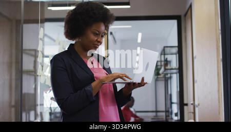 Dactylographier femme d'affaires avec ordinateur portable dans le couloir de bureau, cloison en verre recouverte de notes adhésives jaunes Banque D'Images