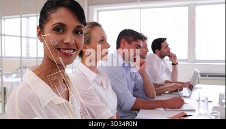 Femme souriante en blouse blanche assise dans la salle de conférence avec des cahiers et des stylos pour ordinateur portable, espace de copie Banque D'Images
