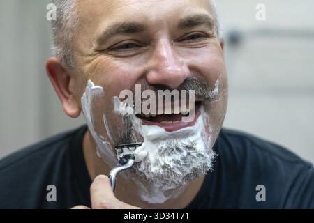 Bel homme rasant sa barbe dans une salle de bain Banque D'Images