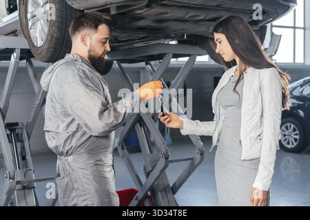 Photo d'Auto Mechanic qui donne les clés de la voiture à sa cliente en atelier au centre de réparation automobile.Qualité de service, satisfaction client Banque D'Images