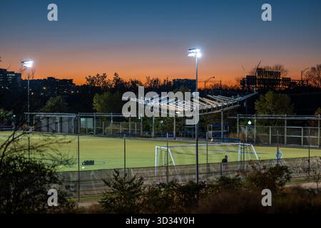 Terrain de football de long Bridge Park Arlington Virginie // ARLINGTON, VIRGINIE — le terrain de football de long Bridge Park est illuminé par les lumières du stade au crépuscule, mettant en valeur son gazon artificiel et ses installations modernes. Le parc présente des auvents architecturaux distinctifs, qui intègrent l'éclairage et potentiellement la technologie solaire, visibles sur le terrain. Long Bridge Park est un parc urbain important à Arlington, en Virginie, aux États-Unis, connu pour ses nombreuses installations sportives et récréatives. Il sert de plaque tournante communautaire importante pour les activités de plein air et les événements sportifs dans la région. Banque D'Images