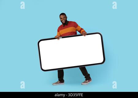 Publicité mobile. Joyeux jeune homme noir portant un grand smartphone vierge Banque D'Images