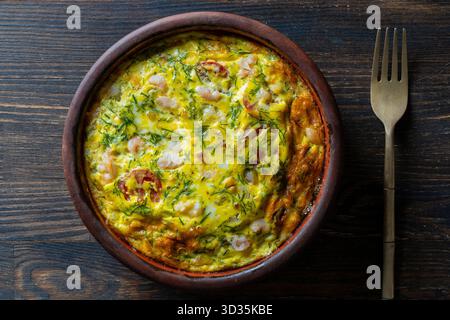 Bol en céramique avec frittata de légumes, nourriture simple. Frittata avec oeuf, tomate, poivre, oignon, crevettes et fromage sur table en bois, gros plan, vue de dessus. I Banque D'Images