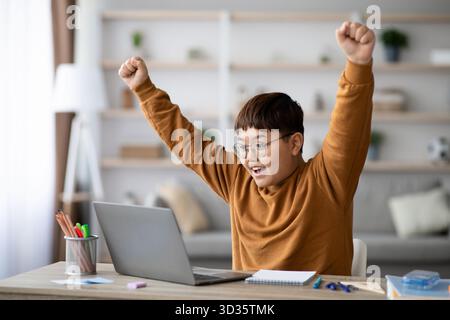 Un écolier asiatique Chubby célèbre heureux sa réussite académique à la maison avec un ordinateur portable et un ordinateur portable Banque D'Images
