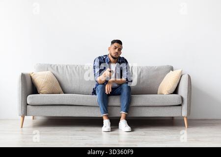 Jeune homme s'ennuyait en regardant la télévision sur un canapé à la maison pendant la soirée Banque D'Images