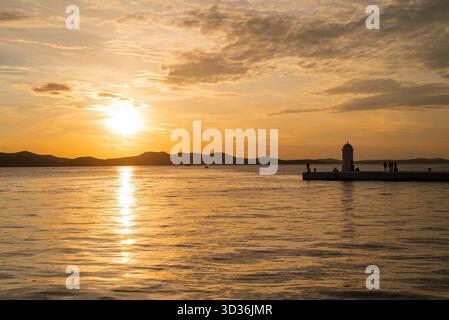 Un beau coucher de soleil sur la promenade du front de mer avec un phare emblématique à Zadar, Croatie. Banque D'Images