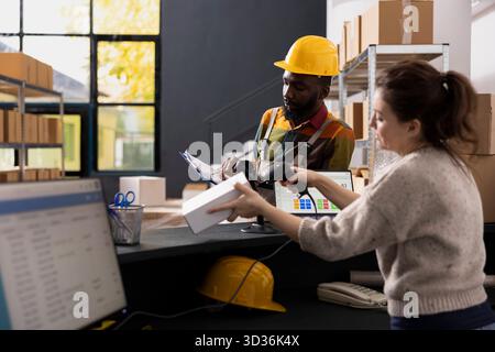 Personnel multiethnique dans les combinaisons vérifiant les colis avec un lecteur de codes-barres, gérant les stocks de stockage et prenant en charge le service d'expédition, la logistique e-shop et la distribution à petite échelle pour les commandes en ligne. Banque D'Images