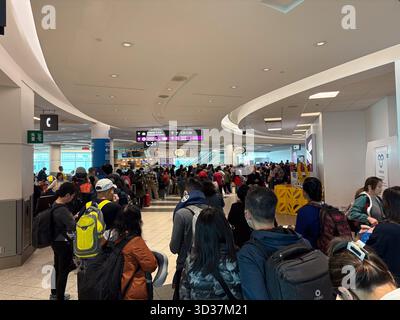 Un grand groupe de passagers fait la queue dans un terminal d'aéroport très fréquenté, attendant de monter à bord d'un avion à une porte. Les panneaux « terminal 1 » et « départs » sont visibles. Banque D'Images