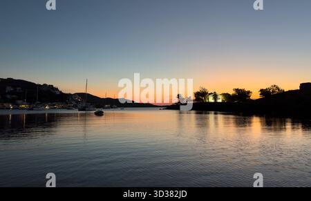 Vue paisible du coucher du soleil sur le port de Vourkari à Kea, également connu sous le nom de Tzia, avec des eaux calmes, des voiliers amarrés, et la lumière chaude du soir se reflétant sur le Ser Banque D'Images