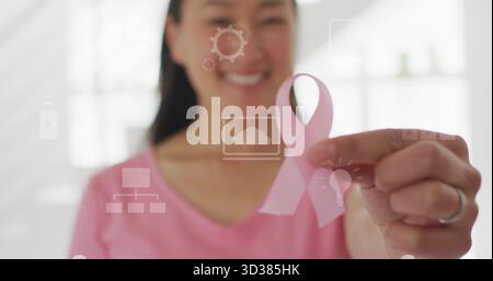 Tenant le ruban de sensibilisation rose dans le bureau, femme coréenne portant une chemise rose avec bague en argent et icônes Banque D'Images
