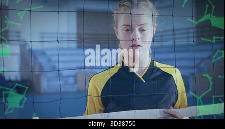 Joueur de volley-ball adolescent debout saisissant le ruban de filet dans la salle de sport de l'école, avec des superpositions vertes Banque D'Images