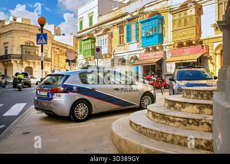 Sliema, Malte - 11.03.2025 : la police patrouille les voitures dans une rue maltaise colorée avec des bâtiments traditionnels, des balcons et des magasins le long de la route. Banque D'Images