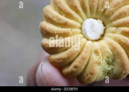 Gros plan de délicieux biscuit au beurre en forme de fleur dorée avec le centre de crème sucrée tenu par le doigt. sucré, savoureux, réconfortant et frais snack maison foo Banque D'Images