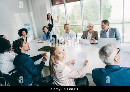 Équipe professionnelle diversifiée collaborant dans une salle de réunion de bureau moderne, discutant des stratégies et des documents commerciaux importants Banque D'Images
