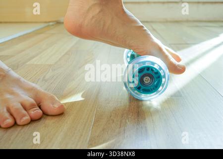Personne pieds nus utilisant un rouleau de massage texturé sur le sol à la maison. Concepts de soins thérapeutiques des pieds, de soulagement de la fasciite plantaire et de routine d'auto-massage. Banque D'Images