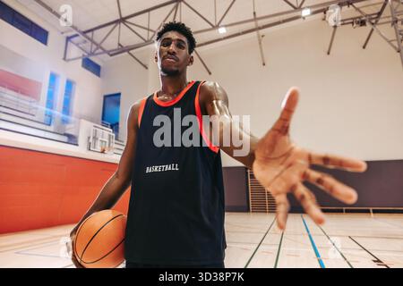 Joueur de basket-ball dans un gymnase tenant un ballon et étendant sa main, montrant l'énergie, la détermination et la confiance dans un sport dynamique et engageant Banque D'Images