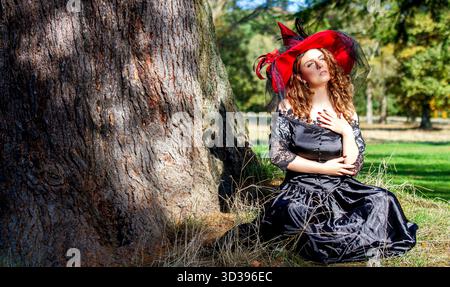 Sorcière femelle en robe noire et chapeau dans le soleil d'automne rude à travers le parc boisé, Écosse Banque D'Images