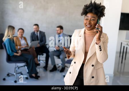 Une femme d'affaires confiante mène sa vie de bureau occupée, multitâche avec la communication smartphone Banque D'Images