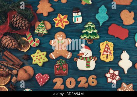 Des biscuits de Noël colorés en forme de bonhommes de neige, d'arbres, d'étoiles et de pain d'épice entourent le texte Joyeux Noël 2026 sur un fond en bois. Banque D'Images