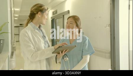 Pointant le médecin dans la blouse de laboratoire guidant l'infirmière regardant la tablette numérique dans le hall de l'hôpital, avec stéthoscope Banque D'Images