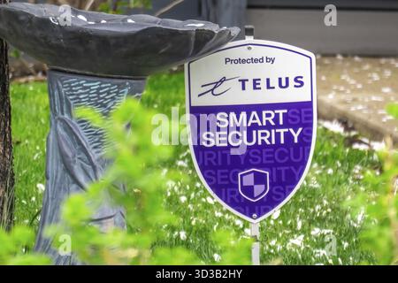 Calgary, Alberta, Canada. 21 mai 2025. Un signe Telus Smart Security monte la garde à côté d'un bain d'oiseaux, un gardien moderne dans un jardin serein, ble Banque D'Images