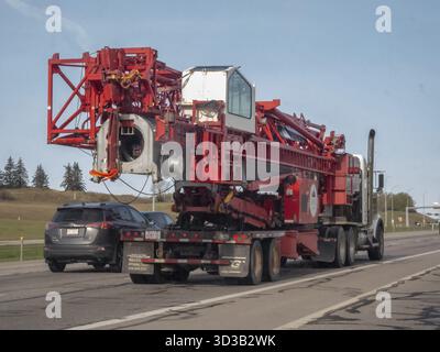 Calgary, Alberta, Canada. 9 mai 2025. Un gros engin de service de grue rouge transporté sur un camion à plateau le long d'une autoroute sous un ciel partiellement nuageux Banque D'Images