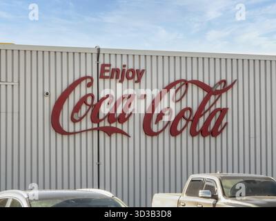 Calgary, Alberta, Canada. 5 avril 2025. Le logo rouge emblématique « Enjoy Coca-Cola » orne l'extérieur en métal ondulé d'un bâtiment, visible au-dessus des voitures stationnées Banque D'Images