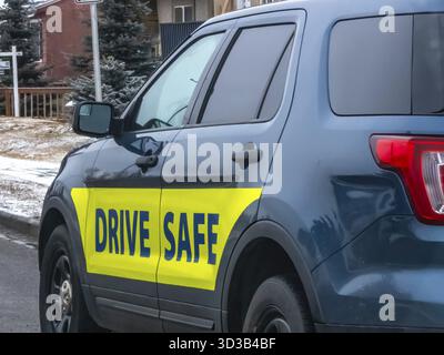 Calgary, Alberta, Canada. 13 mars 2025. Un VUS de police bleu foncé avec un autocollant jaune vif de SÉCURITÉ DE CONDUITE sur son panneau arrière, stationné sur une rue de banlieue enneigée Banque D'Images