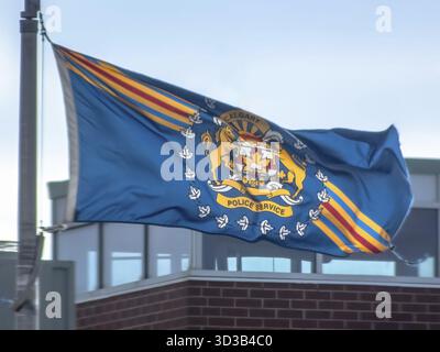 Calgary, Alberta, Canada. 12 mars 2025. Drapeau de la police de Calgary agitant sur un poteau contre un ciel bleu, bâtiment visible ci-dessous. Jour lumineux, emblème avec cheval Banque D'Images