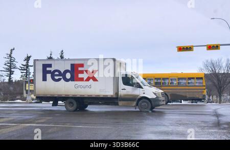 Calgary, Alberta, Canada. 2 mars 2025. Un camion de livraison terrestre FedEx blanc capturé dans un cadre urbain, avec un autobus scolaire jaune en arrière-plan. T Banque D'Images