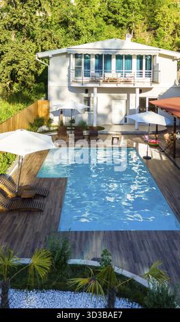 Arrière-cour moderne avec piscine, terrasse en bois et verdure luxuriante entourant une élégante maison de deux étages Banque D'Images