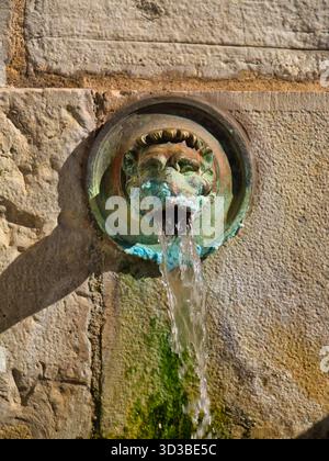 Dax, France - 12 octobre 2025 : de l'eau minérale chaude coule d'un bec à tête de lion avec patine verdigris à la source de la Nehe à Dax, France, capturée dans la lumière chaude de l'après-midi. Banque D'Images