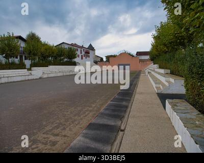 Sare, France - Oct 09 2025 : fronton pelote basque vide avec terrasses blanches sous un ciel sombre à Sare, Pyrénées-Atlantiques, France. Les maisons de village traditionnelles encadrent la cour. Banque D'Images