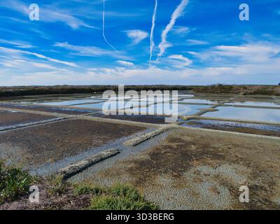 Guérande, France - 01 oct 2025 : les étangs d'évaporation géométriques reflètent un ciel éclatant aux marais salants de Guérande en France, capturant la production traditionnelle de sel marin à midi. Banque D'Images