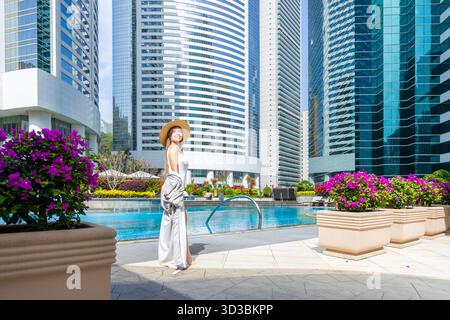 Femme souriant à la piscine portant un chapeau de soleil, gratte-ciel en arrière-plan. Urbain Banque D'Images