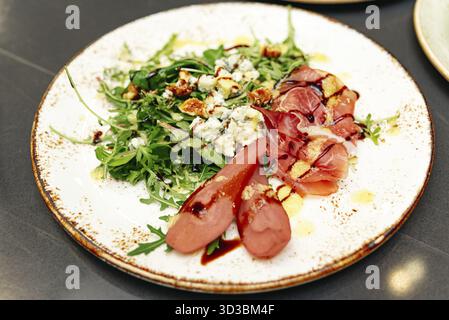 Nourriture, Une salade gourmande avec roquette fraîche, poires pochées, prosciutto, fromage bleu, noix confites, et glaçage balsamique, élégamment plaqué sur un ce rustique Banque D'Images