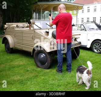 Bad Bentheim, Allemagne - 13 juillet 2025 Un homme avec un chien photographie une Volkswagen type 82 Kübelwagen avec son smartphone lors d'une rencontre de voitures anciennes Banque D'Images