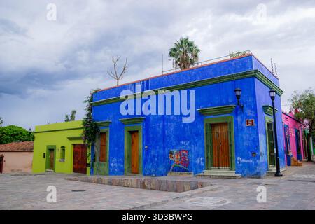 Maisons coloniales peintes en bleu électrique et vert citron avec des portes en bois, dans une rue historique d'Oaxaca, au Mexique, sous un ciel nuageux. Banque D'Images