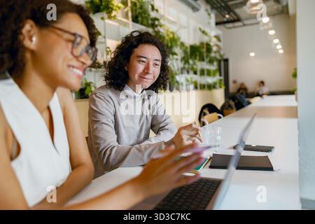 les membres de l'équipe énergiques échangent des idées tout en travaillant sur des maquettes numériques dans un environnement de café dynamique Banque D'Images