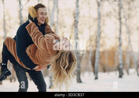 Un jeune couple aimant jouant à pied et s'amusant dans un parc forestier d'hiver Banque D'Images