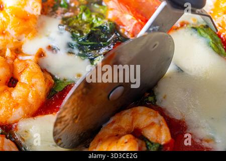 Pizza avec tomates et crevettes est coupée avec un couteau spécial. Gros plan. Photo de haute qualité Banque D'Images