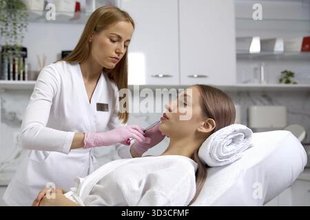 Procédure rajeunissante d'injections faciales pour resserrer et lisser les rides sur la peau du visage d'une belle jeune femme dans un salon de beauté Banque D'Images