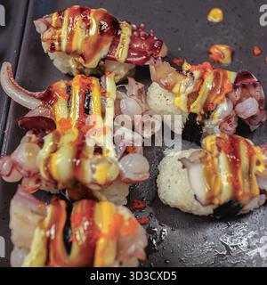 Pieuvre nigiri de style fusion avec mayonnaise pimentée épicée et tobiko rouge, servie sur un plateau noir. Hors-d'œuvre de fruits de mer asiatiques haut de gamme pour le tourisme culinaire. Banque D'Images