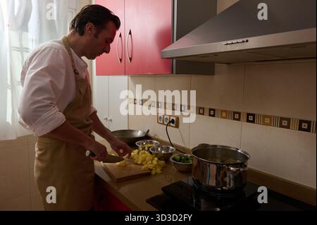 Un père dévoué coupe des pommes de terre et mijote la soupe tandis que sa fille aide au comptoir dans une cuisine lumineuse, partageant la préparation des repas de famille et chaud, hom Banque D'Images